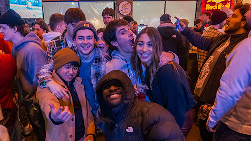 Five college students, surrounded by many other students, pose for a photo at the College Daze party.